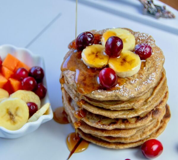 Stack of pancakes topped with bananas and cherries, drizzled with syrup, perfect for breakfast.