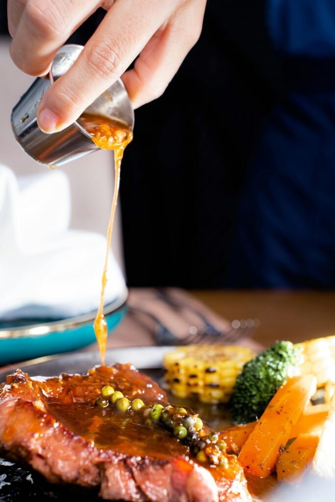 Close-up of steak with peppercorn sauce being poured, accompanied by vegetables, showcasing gourmet dining.