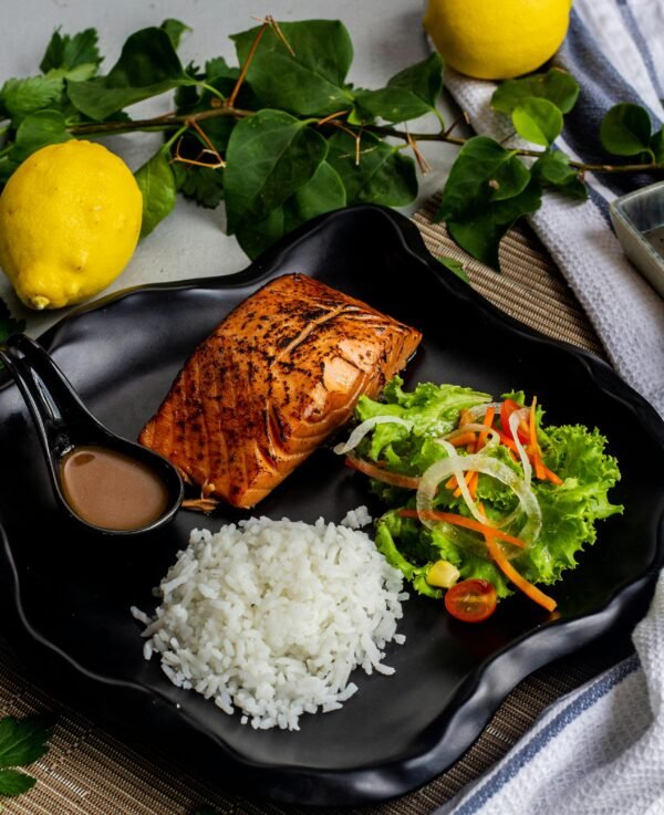 Delicious grilled salmon with rice and fresh salad on a stylish black plate.